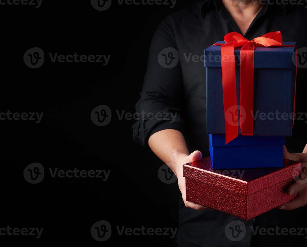 adult man in a black shirt holds in his hands a stack of paper-wrapped gifts photo