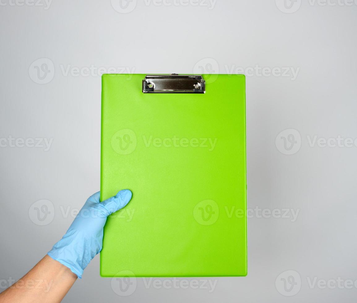 female hand with blue medical glove holding a green tablet for clamping papers photo