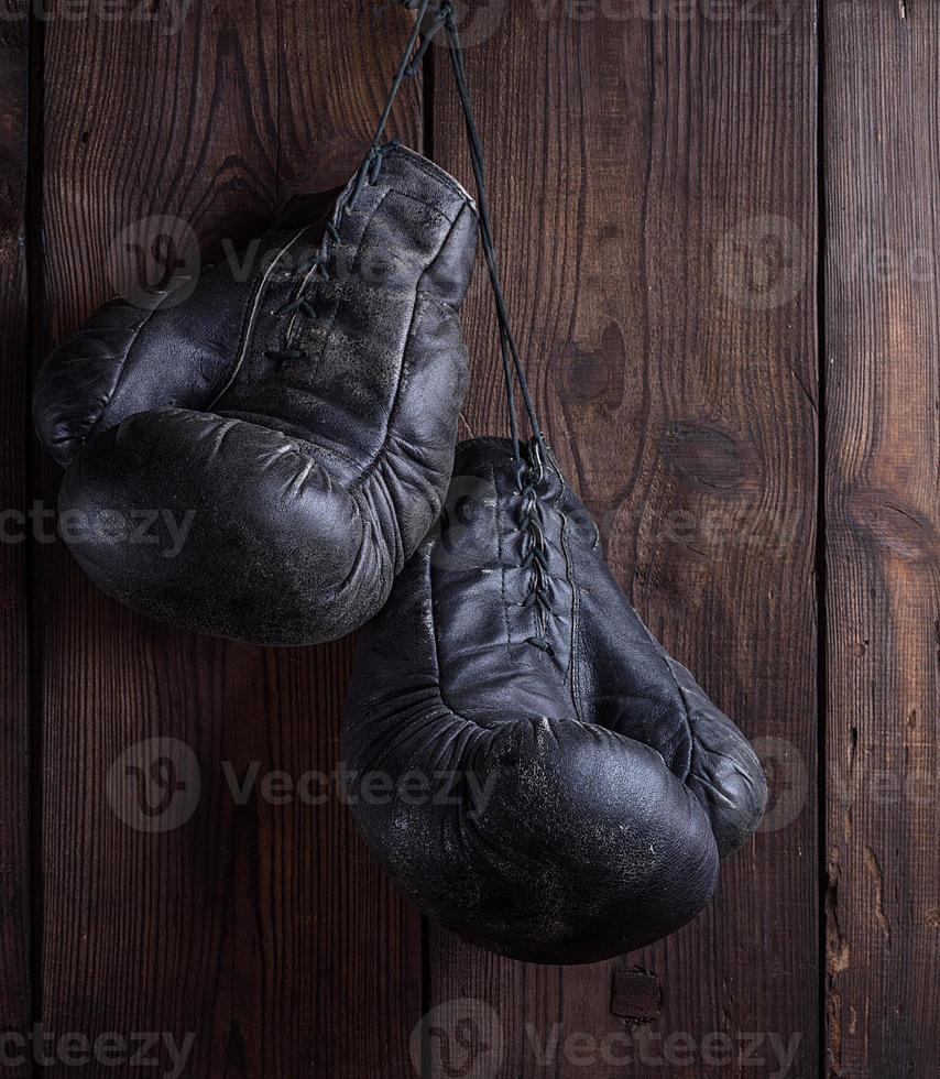 pair of very old shabby black leather boxing gloves hanging on a nail photo