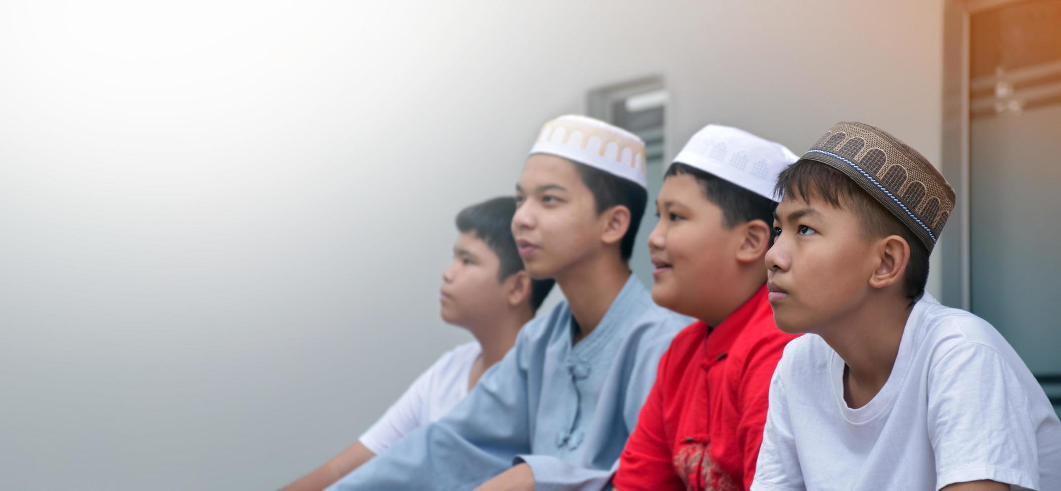 Asian muslim or islamic boys sitting with muslim boys in a row to pray or to do the religious activity, soft and selective focus. photo