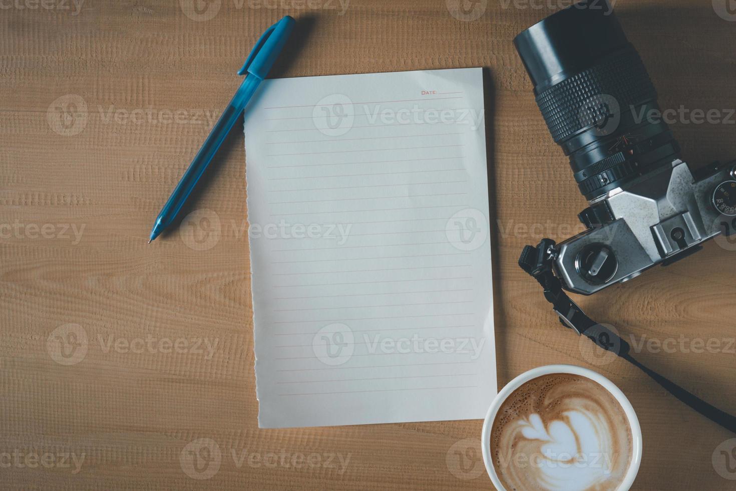 vista superior de papel vacío, taza de café, cámara y bolígrafo en la mesa de madera foto