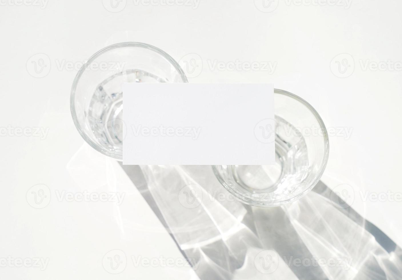 Blank business card mockup on glass with shade of natural leaves shadow overlay on white background, for product or presentation photo