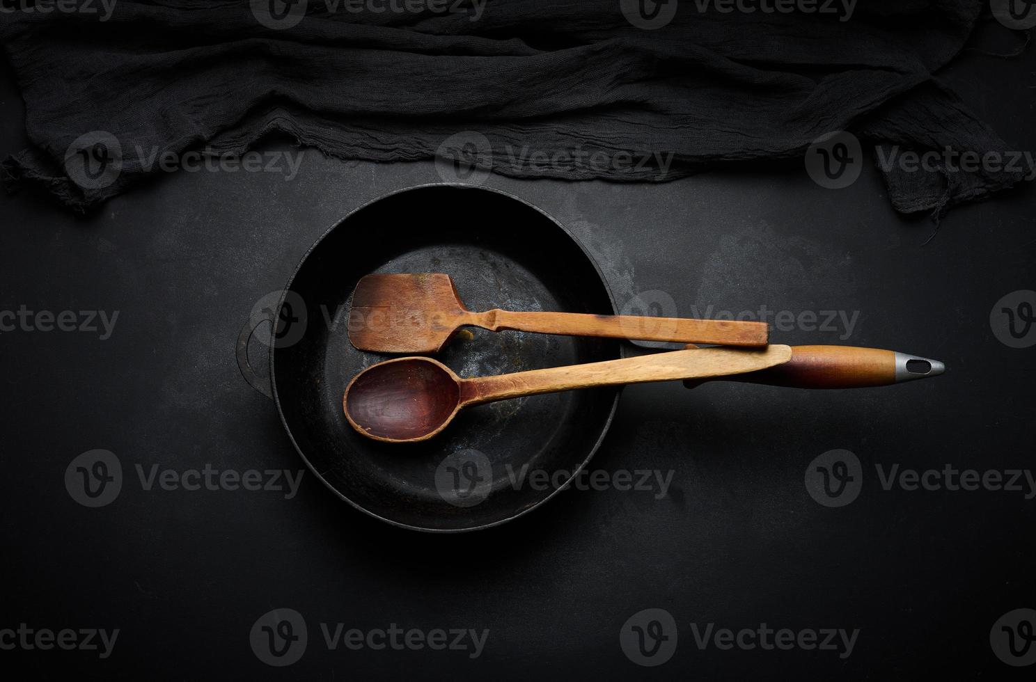 Empty round cast iron frying pan with wooden handle on black table, top view photo