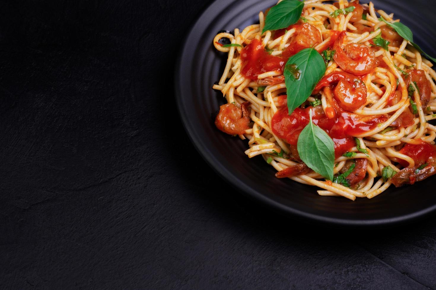 deliciosa pasta de espagueti con gambas y queso servida en un plato negro sobre una mesa de fondo negro receta italiana, salsa de tomate, verduras y especias vista superior con espacio para copiar foto