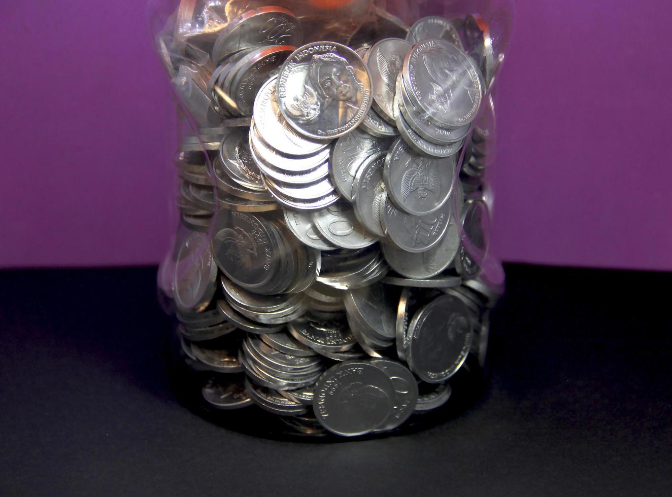 Central Jakarta, Indonesia - December 13th, 2022 - Plastic jar full of Indonesian rupiah money coin. Photo isolated on plain background. Investing or financial saving themed image.