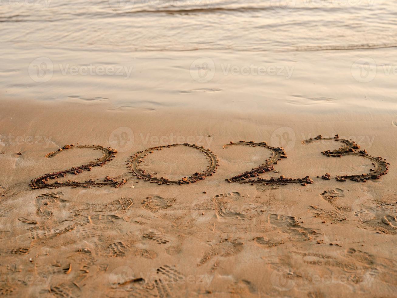 New year concept photo. Numbers 2023 handwritten in the sand surface. Soft sea wave and beach on background. photo