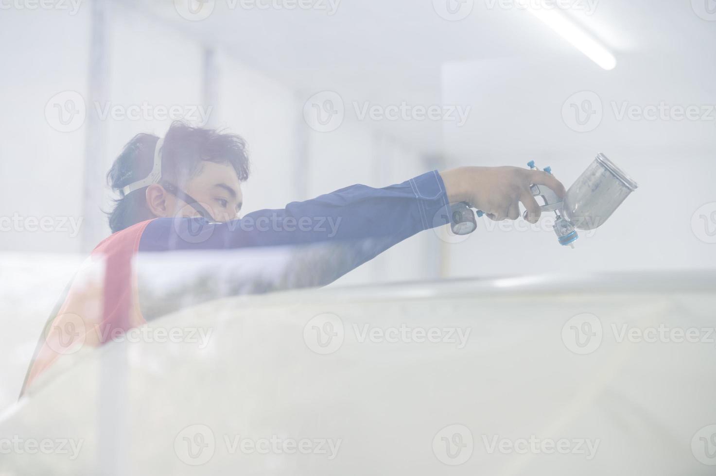 Asian auto mechanic wearing protective suit and respirator paints car body bumpers in paint room,spraying cars in paint room photo