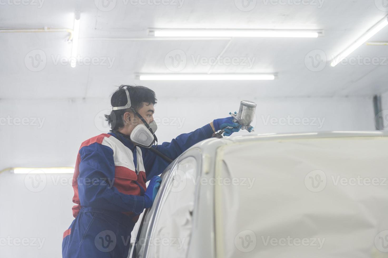 Asian auto mechanic wearing protective suit and respirator paints car body bumpers in paint room,spraying cars in paint room photo