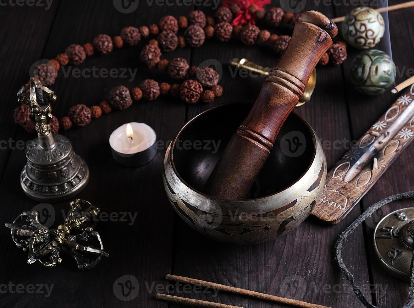 copper singing bowl and a wooden stick on a brown table photo