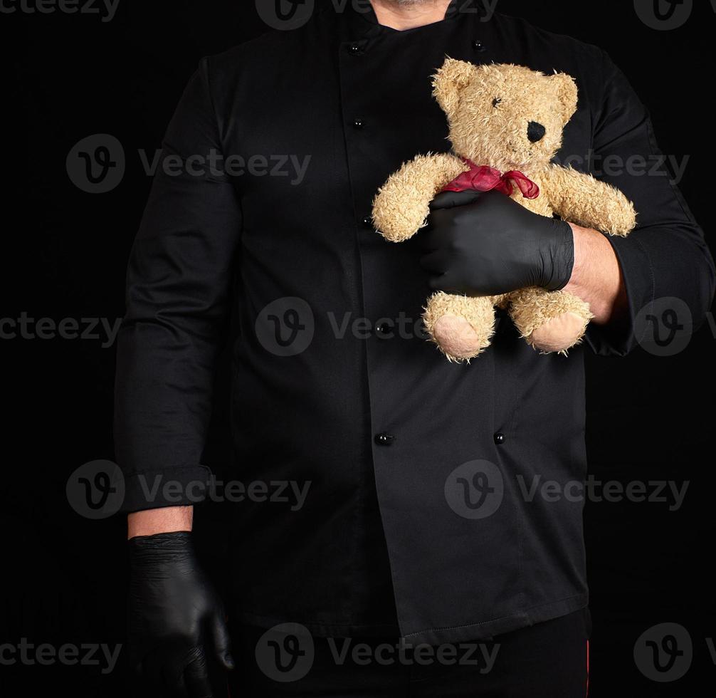 man in a black uniform holds in his hand a toy teddy bear photo