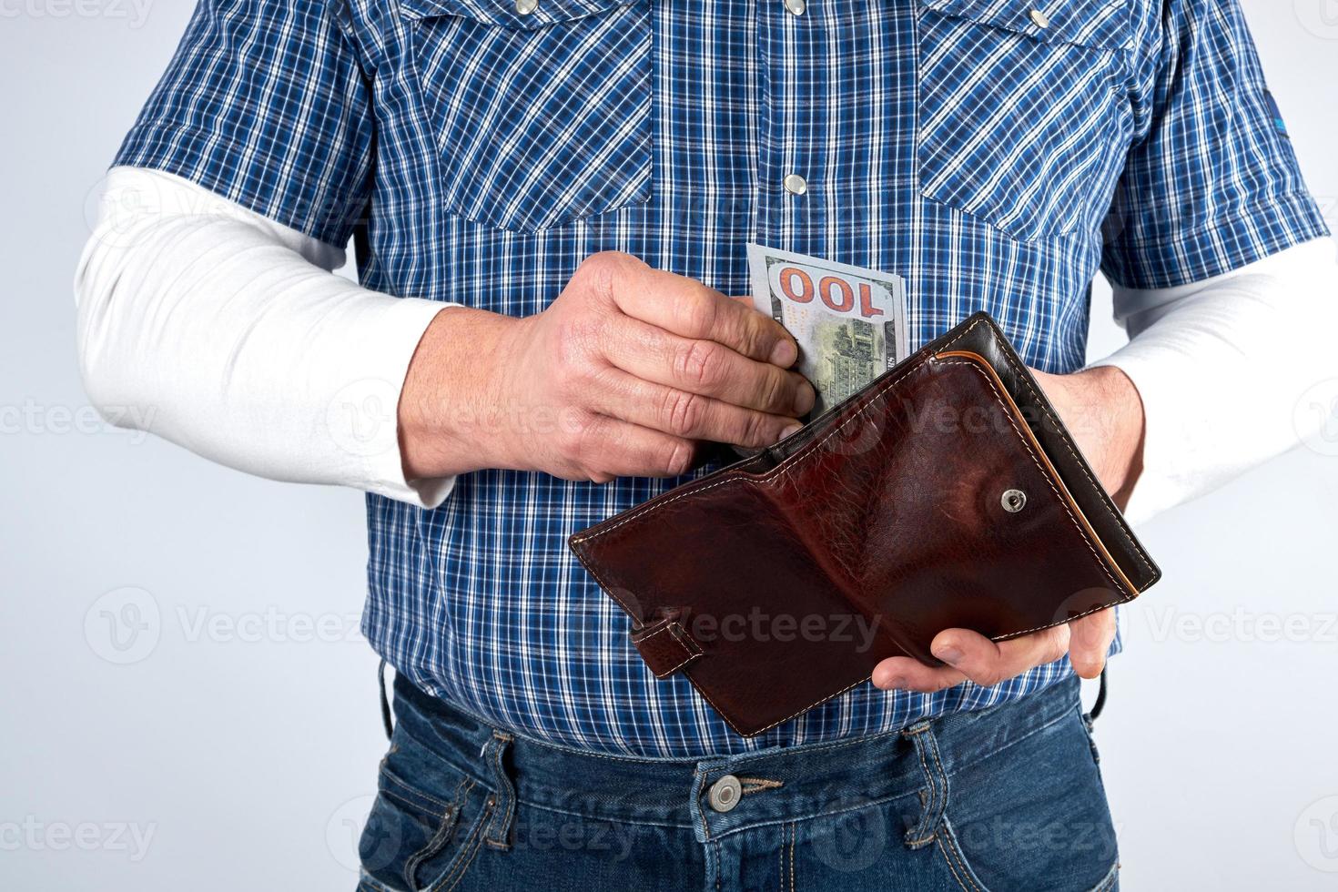 man in a blue plaid shirt and jeans holds a brown leather purse photo
