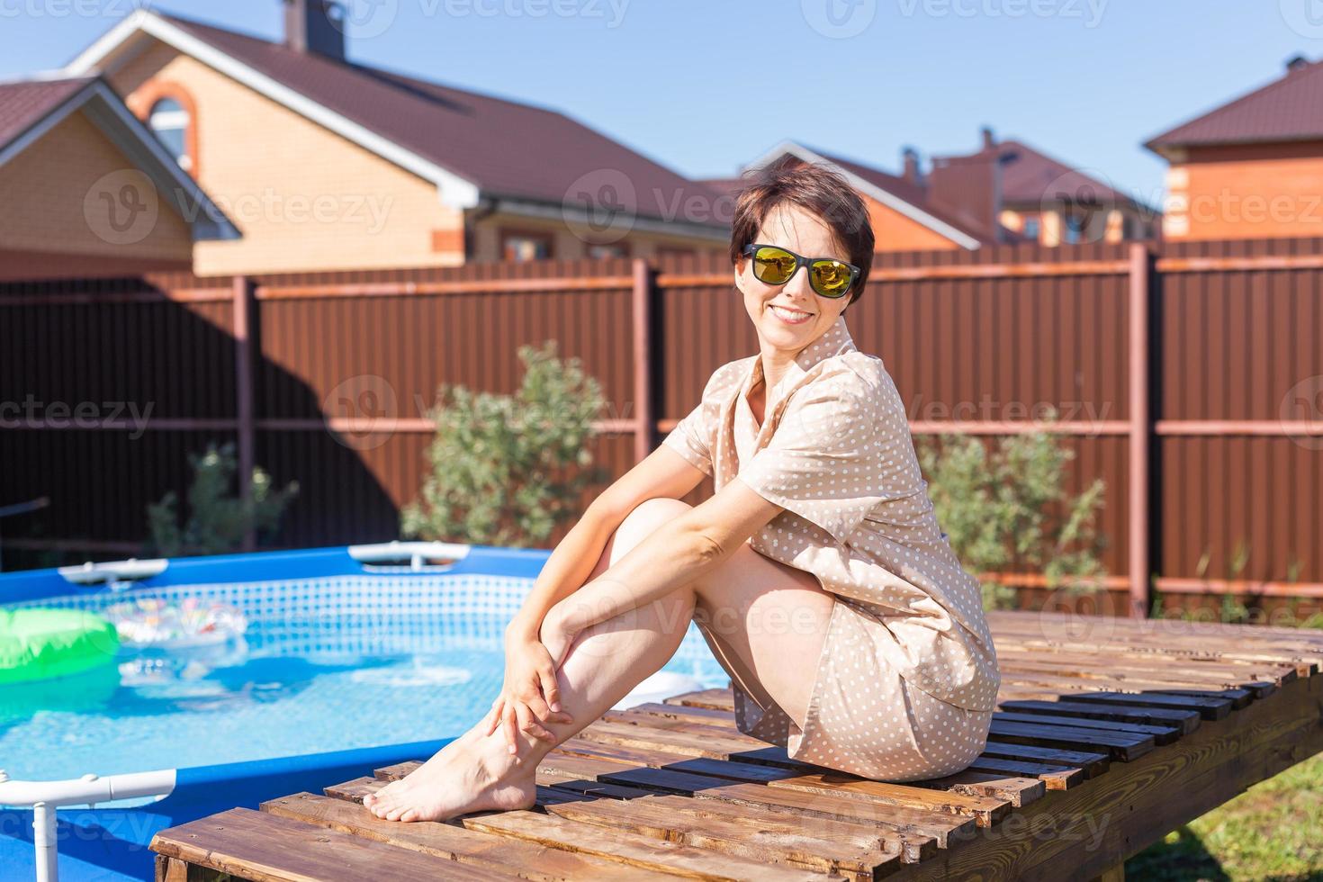 Portrait of pretty young woman in pajama sitting near inflatable swimming pool - summer and country life concept photo