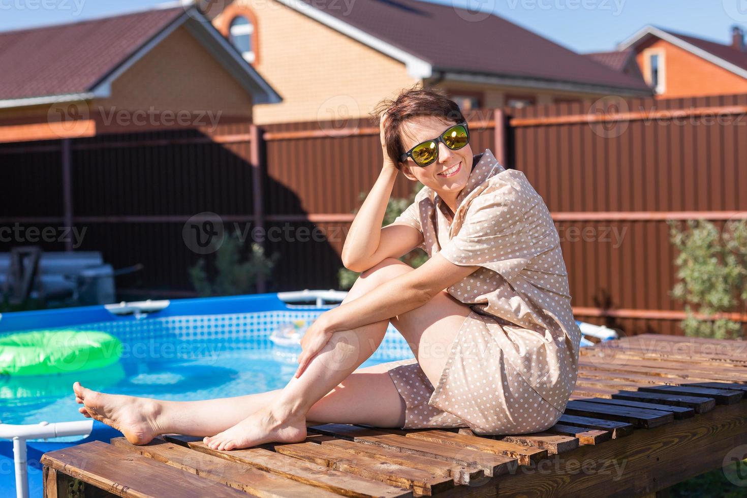 Portrait of pretty young woman in pajama sitting near inflatable swimming pool - summer and country life concept photo