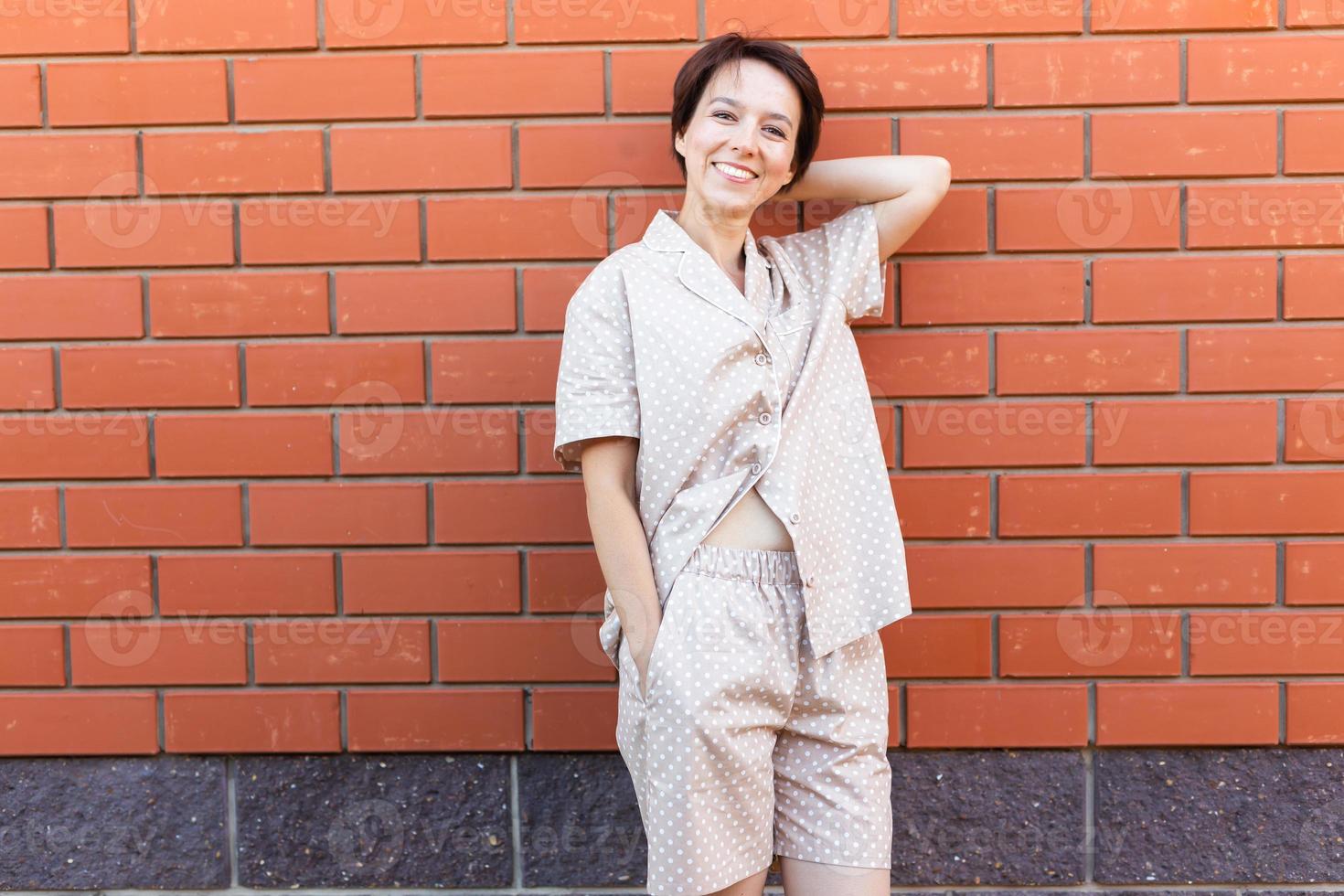 Cheerful woman in home wear pajama outdoor brick wall background emotions copy space and empty place for text - sleepwear and homewear concept photo
