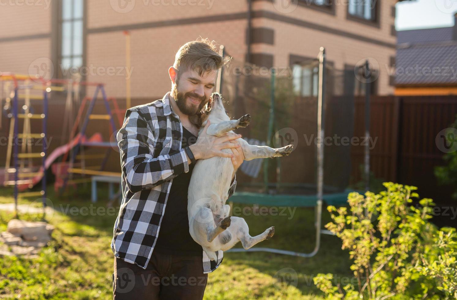 Young man holding jack russell terrier dog near his house on backyard - pet owner and animal photo