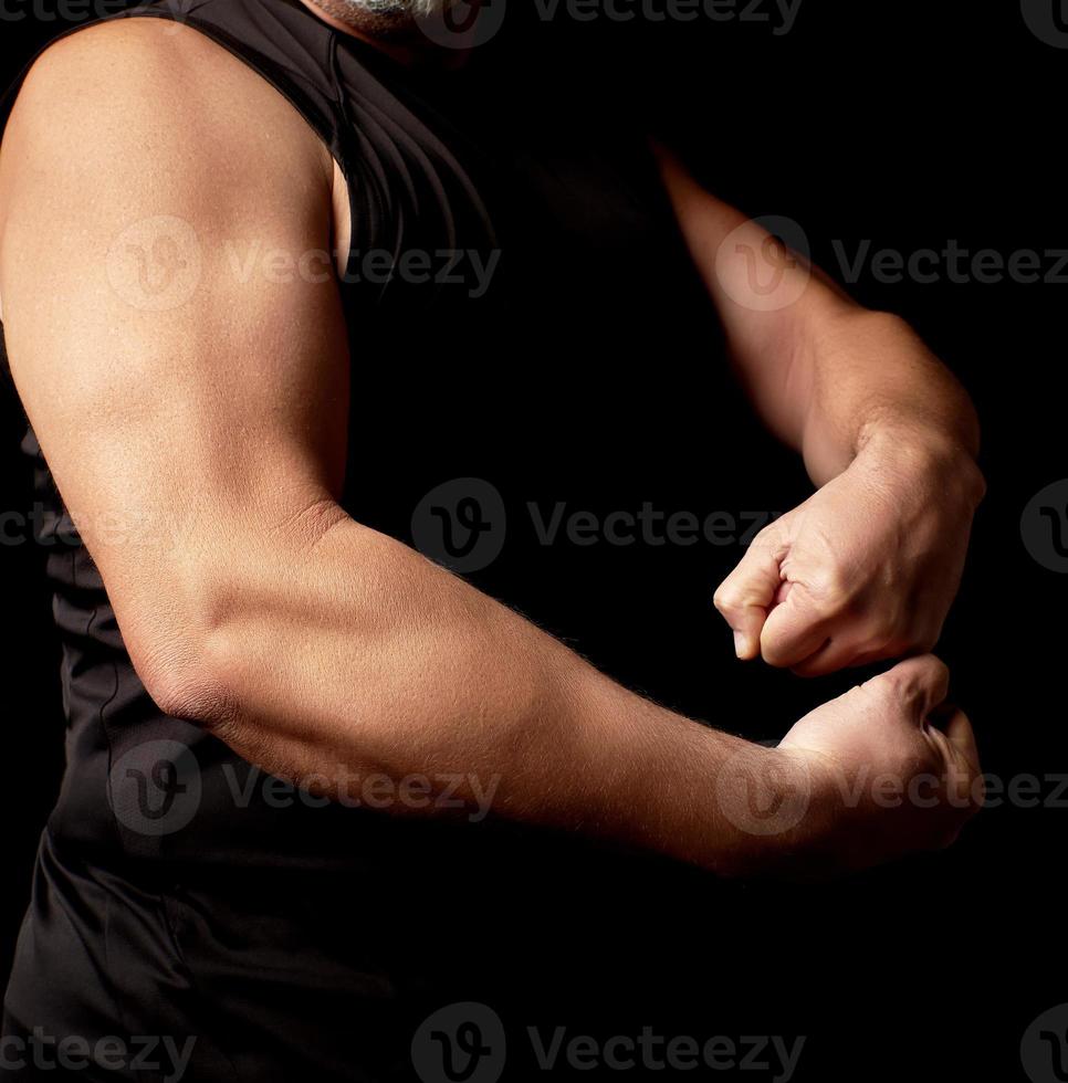 adult man with a sports figure in black clothes strained his muscles in his arms photo