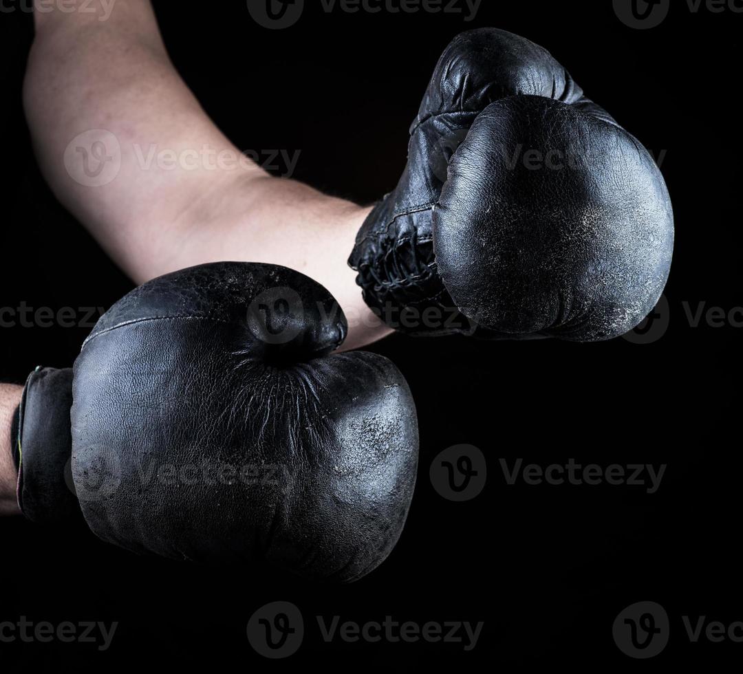 men's hands are wearing old leather black boxing gloves photo