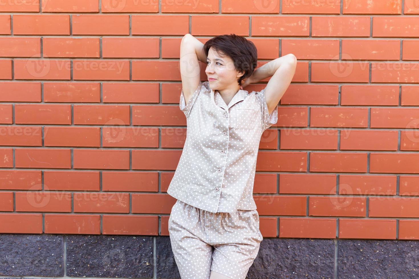 Cheerful woman in home wear pajama outdoor brick wall background emotions copy space and empty place for text - sleepwear and homewear concept photo