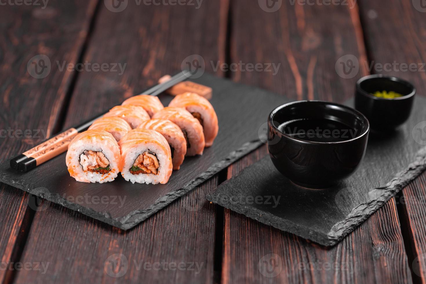 rollo de sushi maguro con salmón, anguila ahumada, aguacate y tobiko en primer plano de pizarra negra. menú de sushi comida japonesa. foto