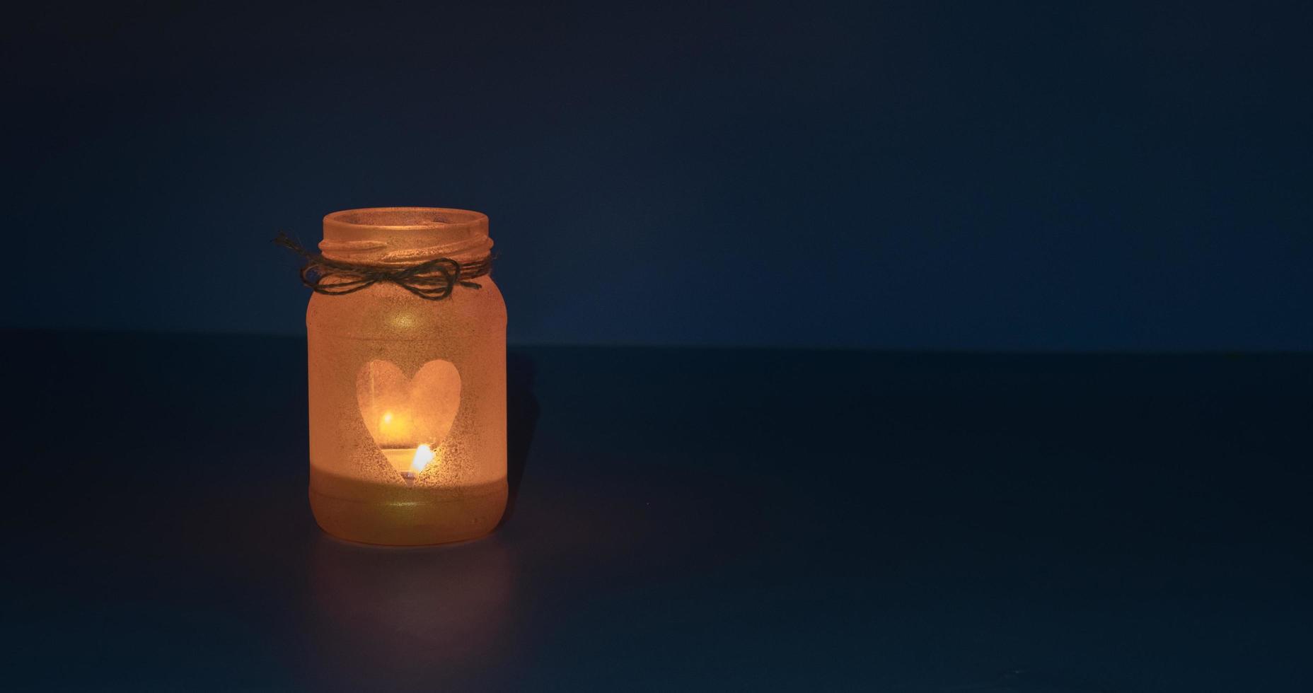 frasco de vidrio con llama de vela en forma de corazón en la oscuridad foto