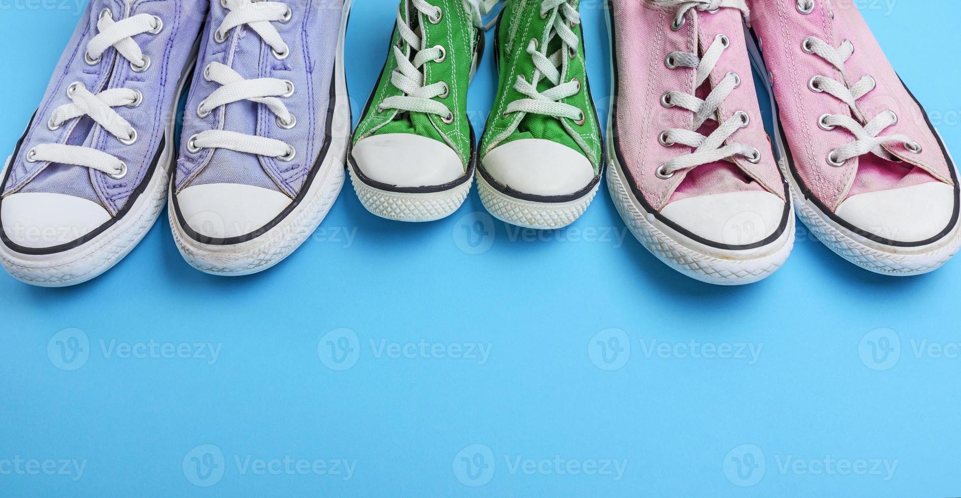 three pair of old worn textile sneakers on a blue background photo