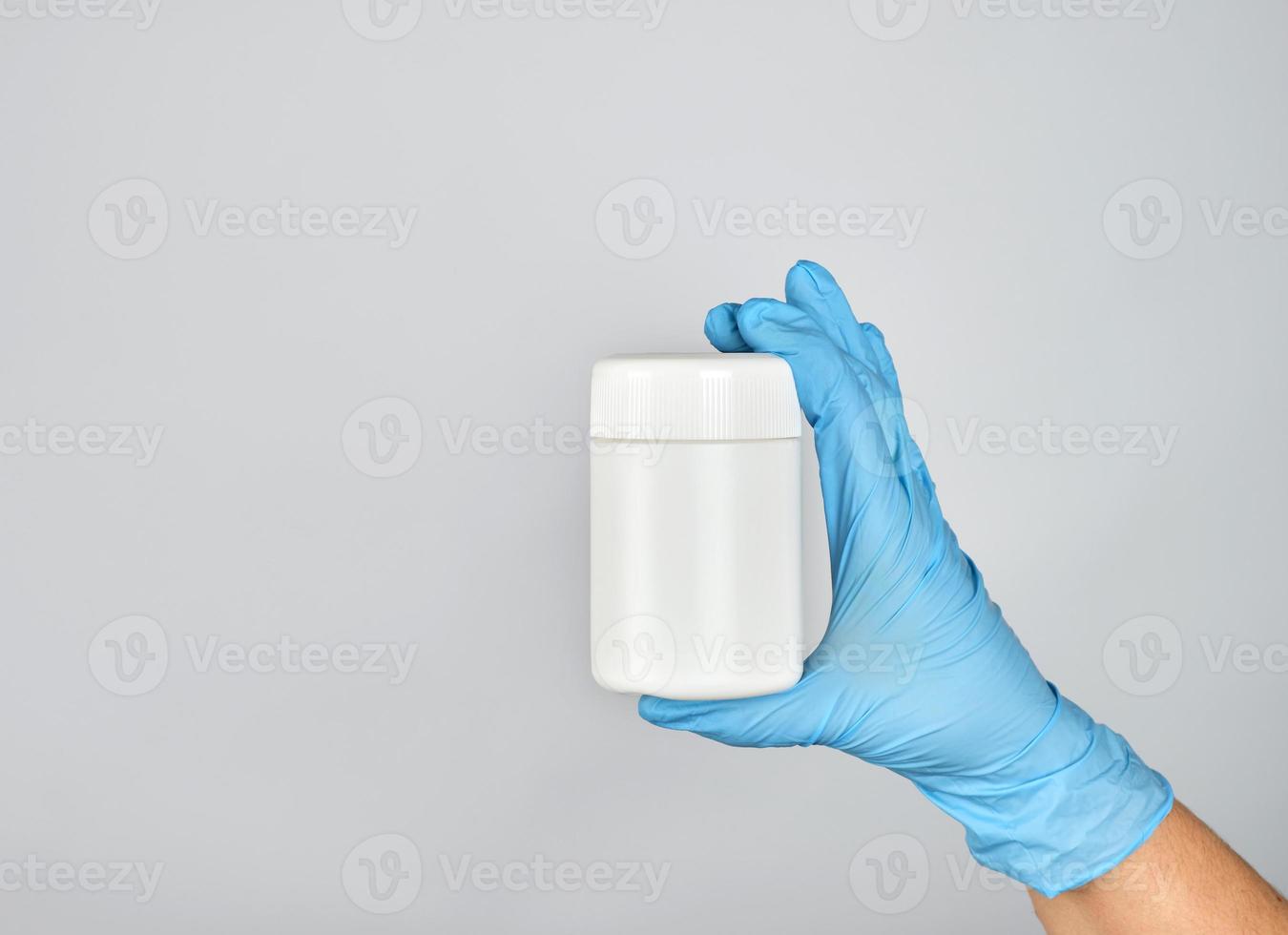 hand in blue sterile glove holds white plastic jar with pills photo