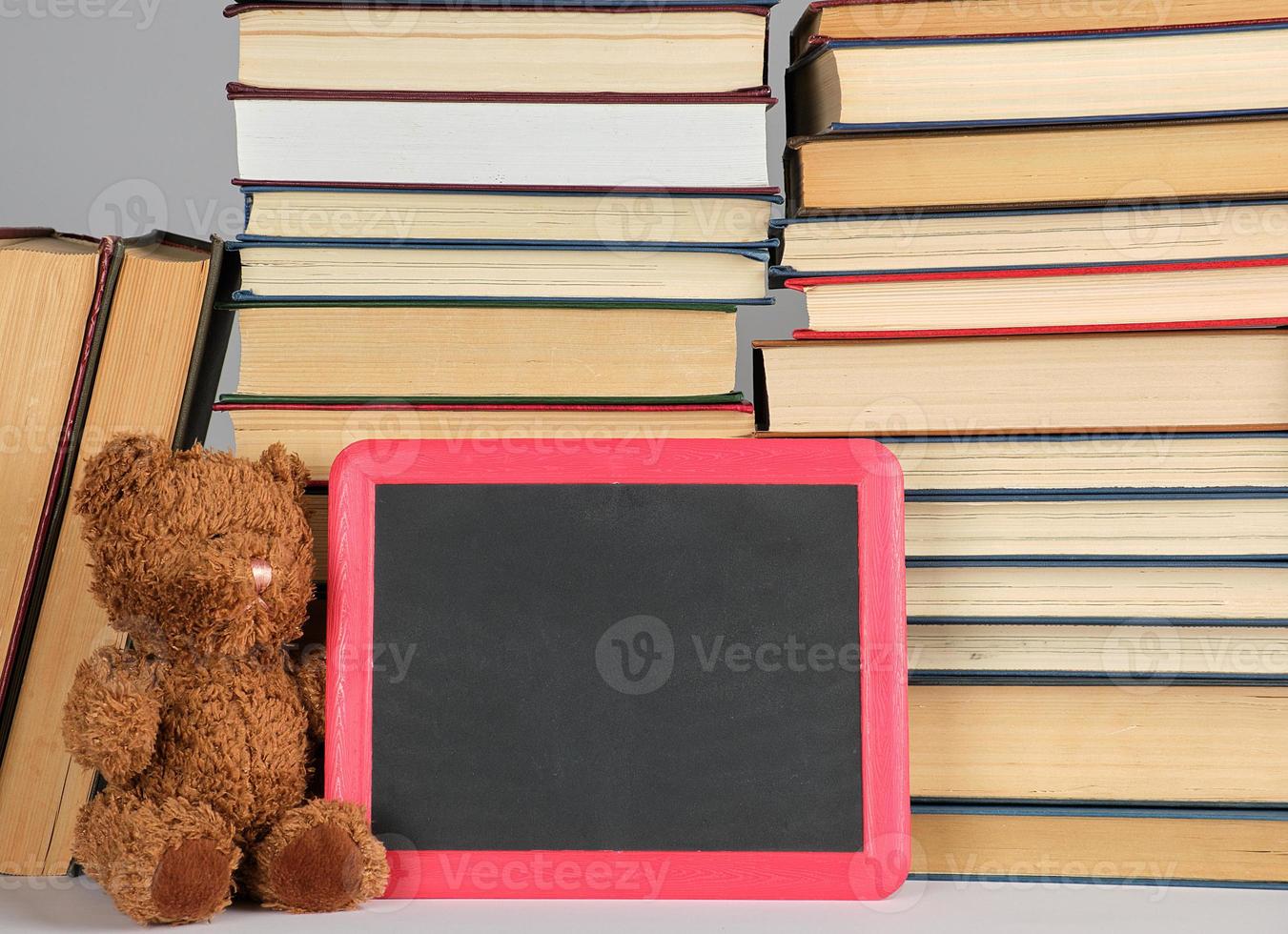 brown teddy bear and empty black board in red frame on the background of pile of books photo
