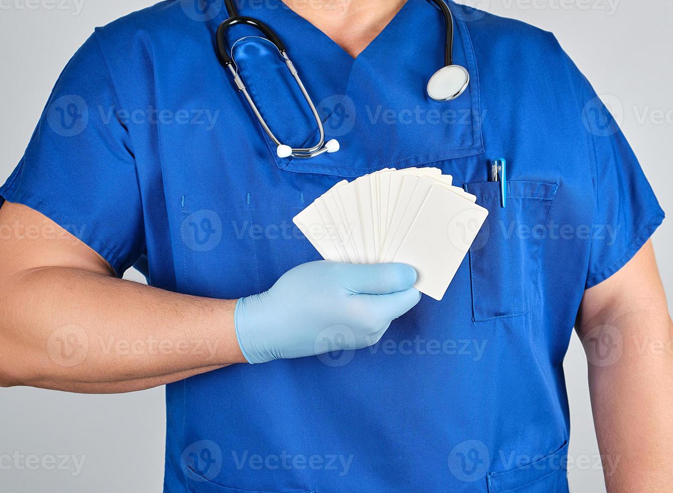 doctor in sterile latex gloves and blue uniform holds a blank white business card photo