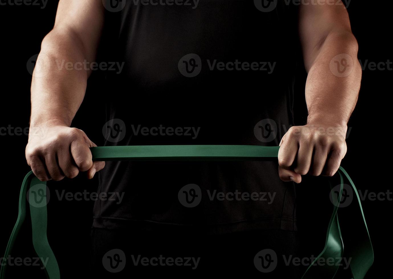 athlete with a muscular body in black clothes is doing physical exercises with green rubber photo