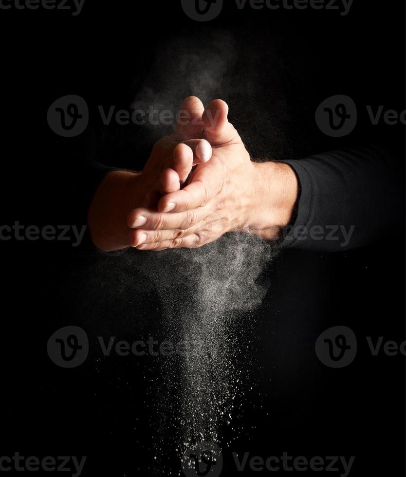 man claps his hands and scatters to the side a white substance on a black background photo