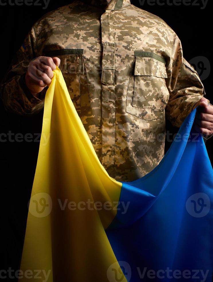 soldado ucraniano sostiene en su mano la bandera amarilla-azul del estado foto