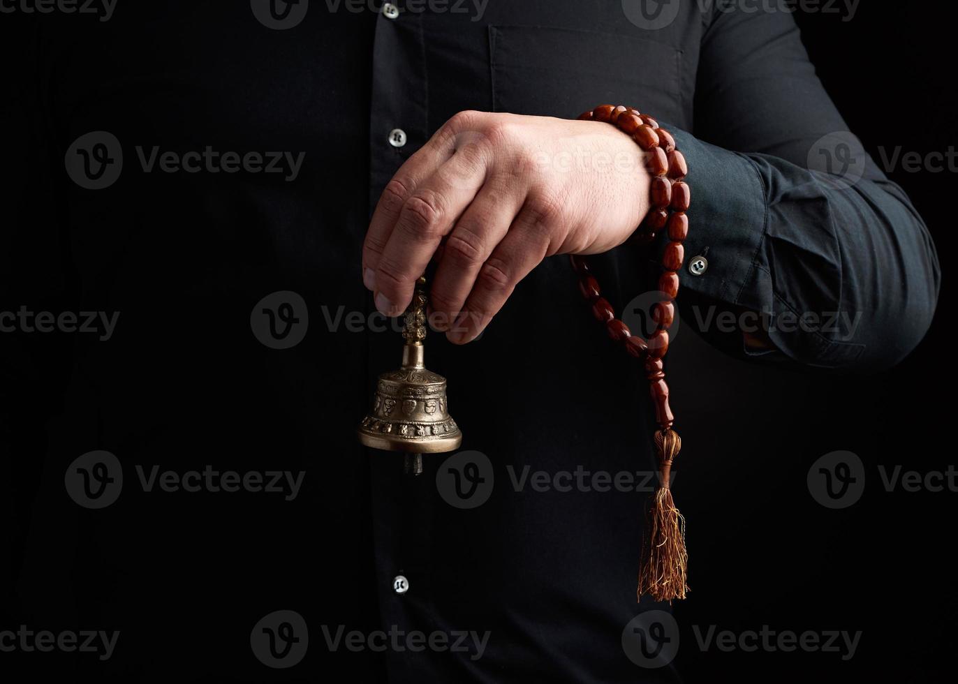 adult man in a black shirt holds a copper Tibetan ritual bell, low key photo