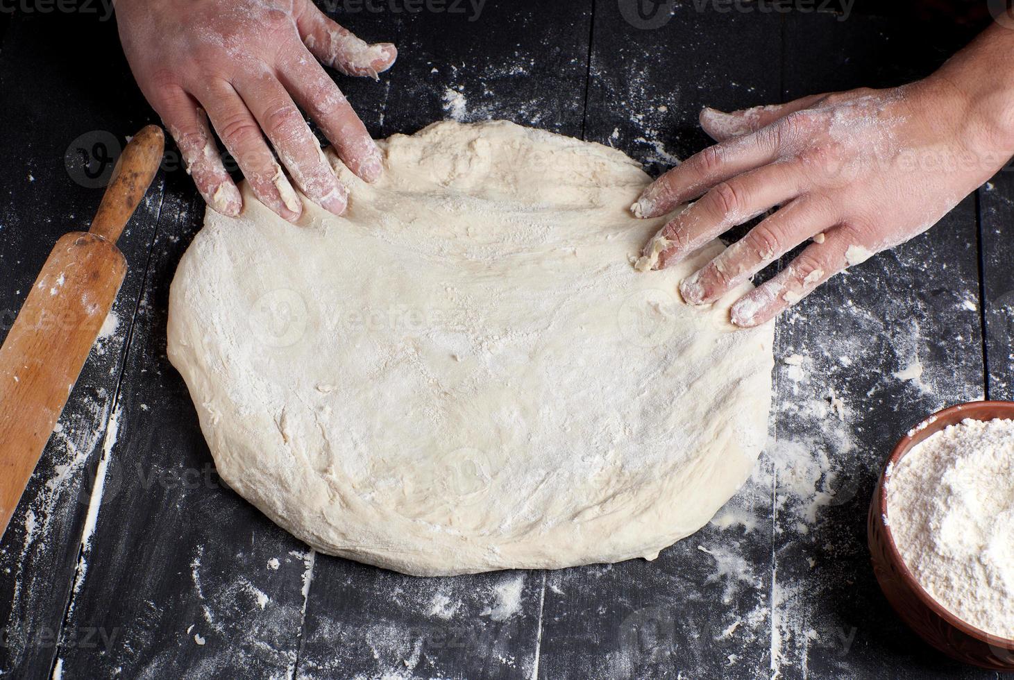 las manos de los hombres amasan una masa redonda para hacer pizza foto