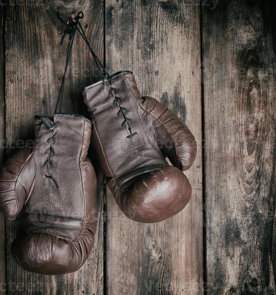 very old leather brown boxing gloves hang on an old shabby wooden wall photo