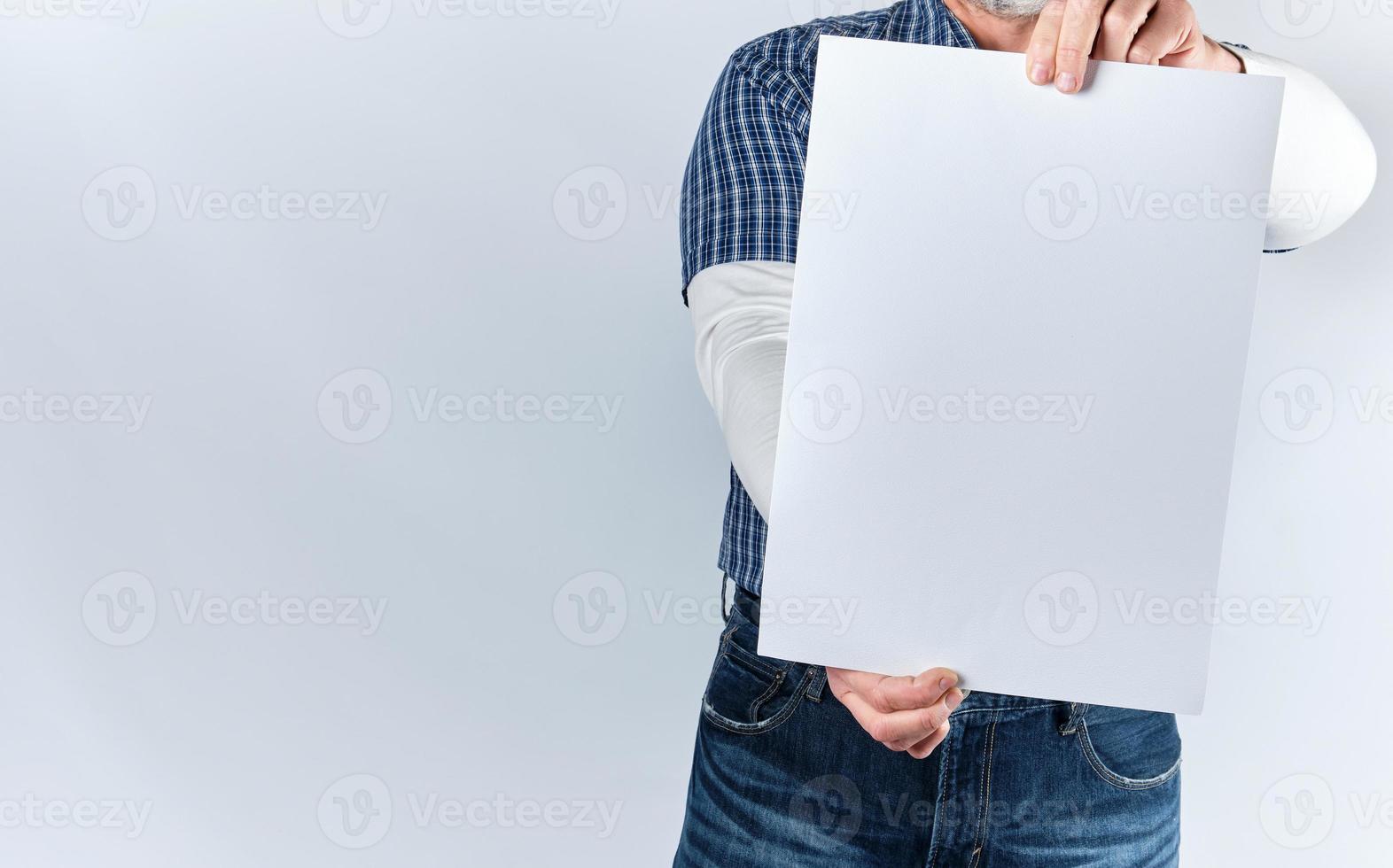 man in a blue plaid shirt and jeans is holding a blank rectangular white paper sheet photo