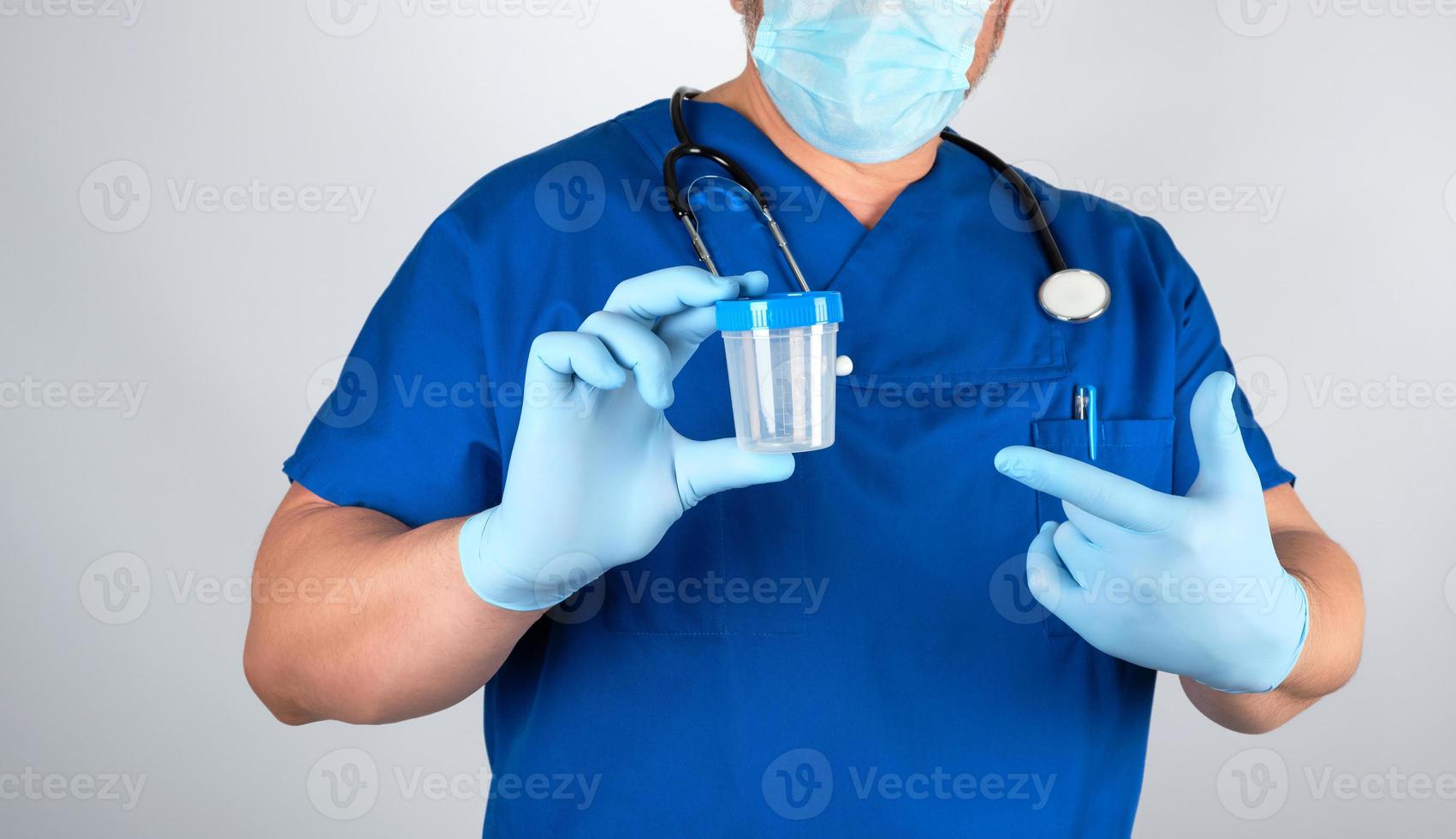 doctor in blue uniform and latex gloves is holding an empty plastic container for taking urine samples photo