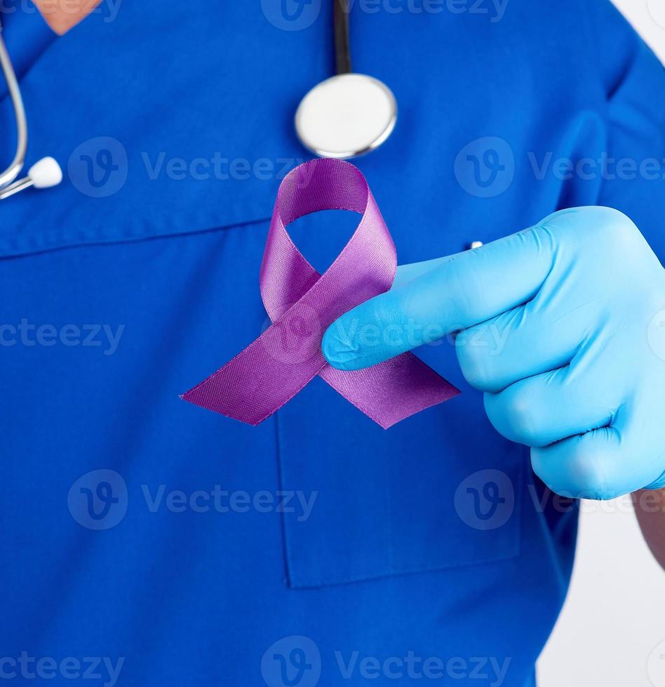doctor in blue uniform and latex gloves holds a purple ribbon as a symbol of early research and disease control photo