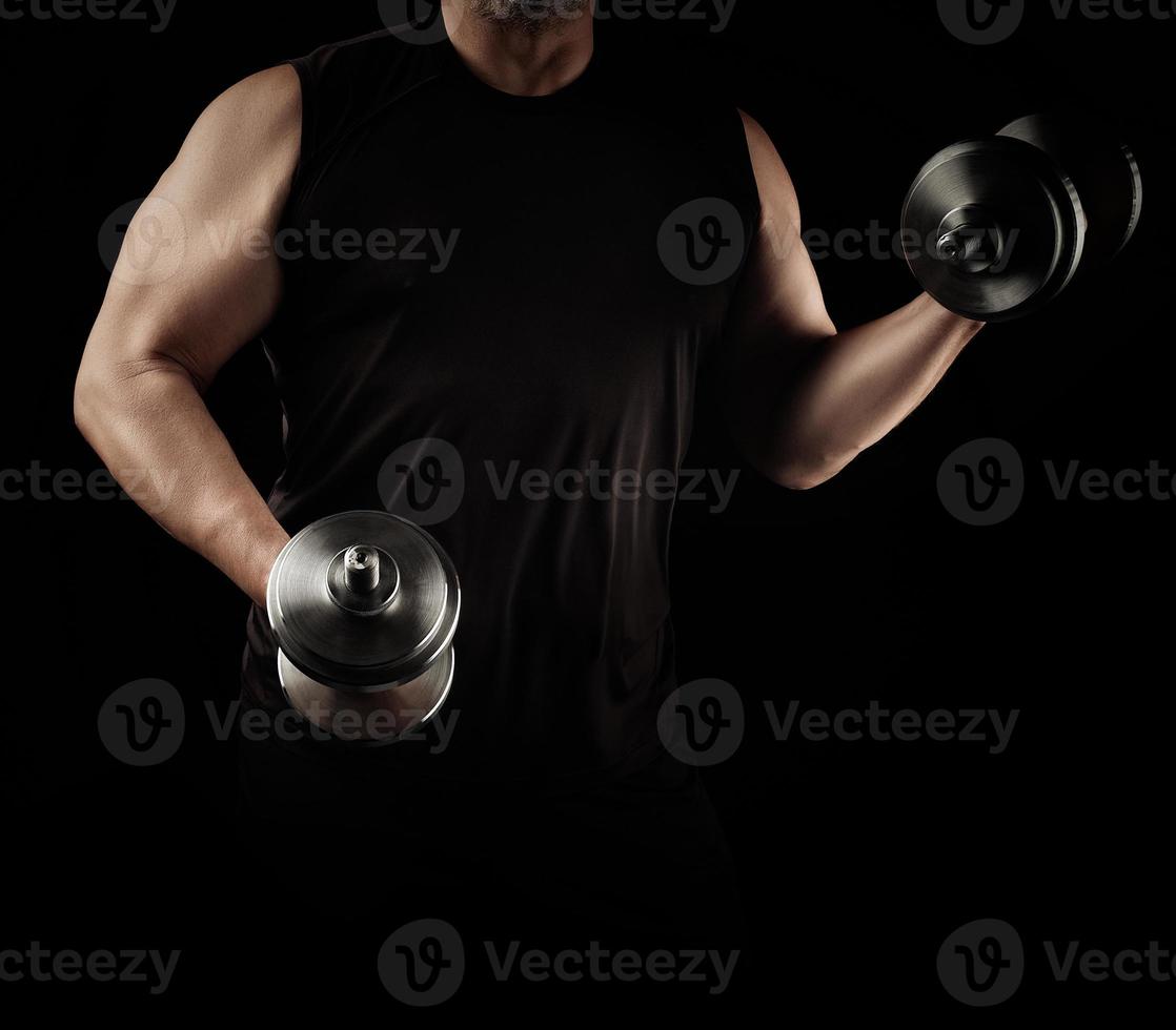 man in black clothes holds steel dumbbells in his hands, his muscles are tense photo