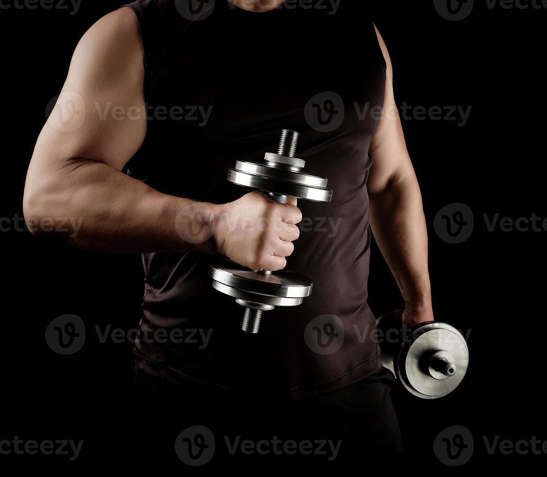 man in black clothes holds steel dumbbells in his hands, his muscles are tense photo