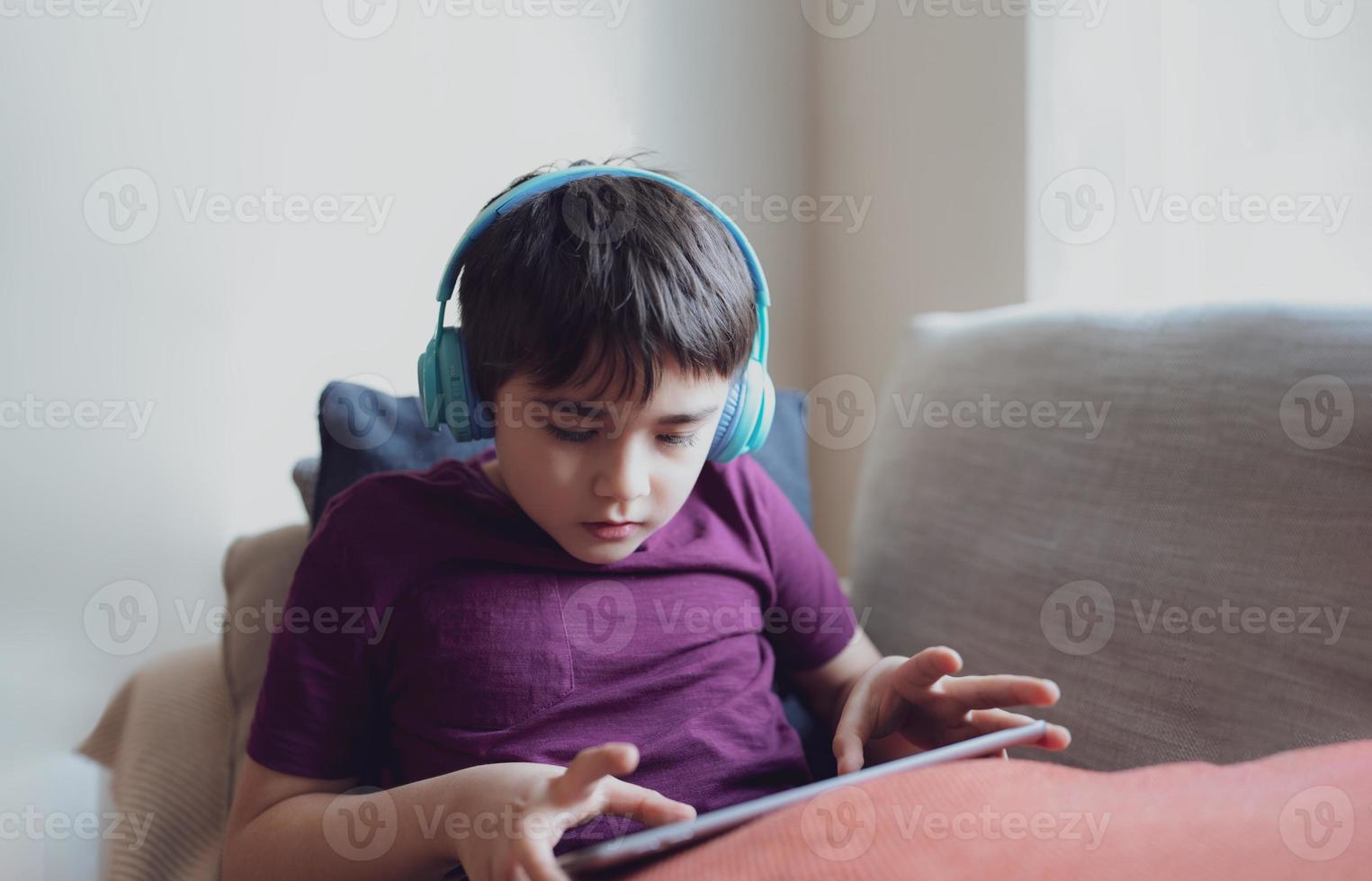 Education concept,High key portrait primary school Kid reading E-book on tablet for homework,Child wearing headphone playing game online on internet,boy sitting on sofa watching cartoon on digital pad photo