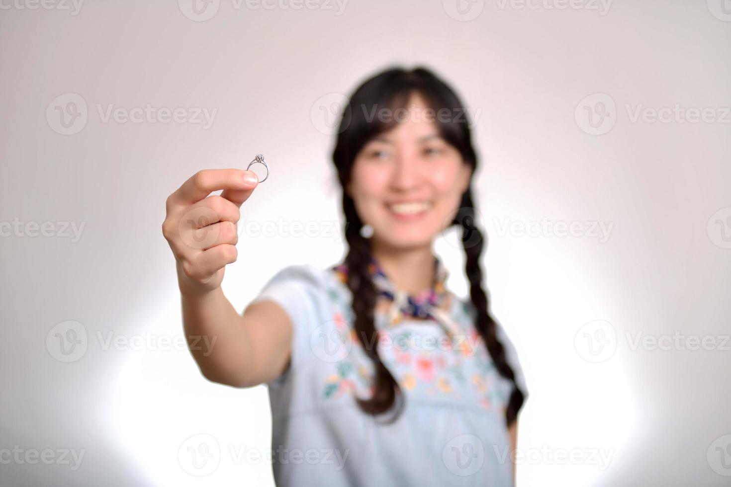 retrato de una hermosa joven asiática vestida de denim sosteniendo un anillo de compromiso con fondo blanco foto