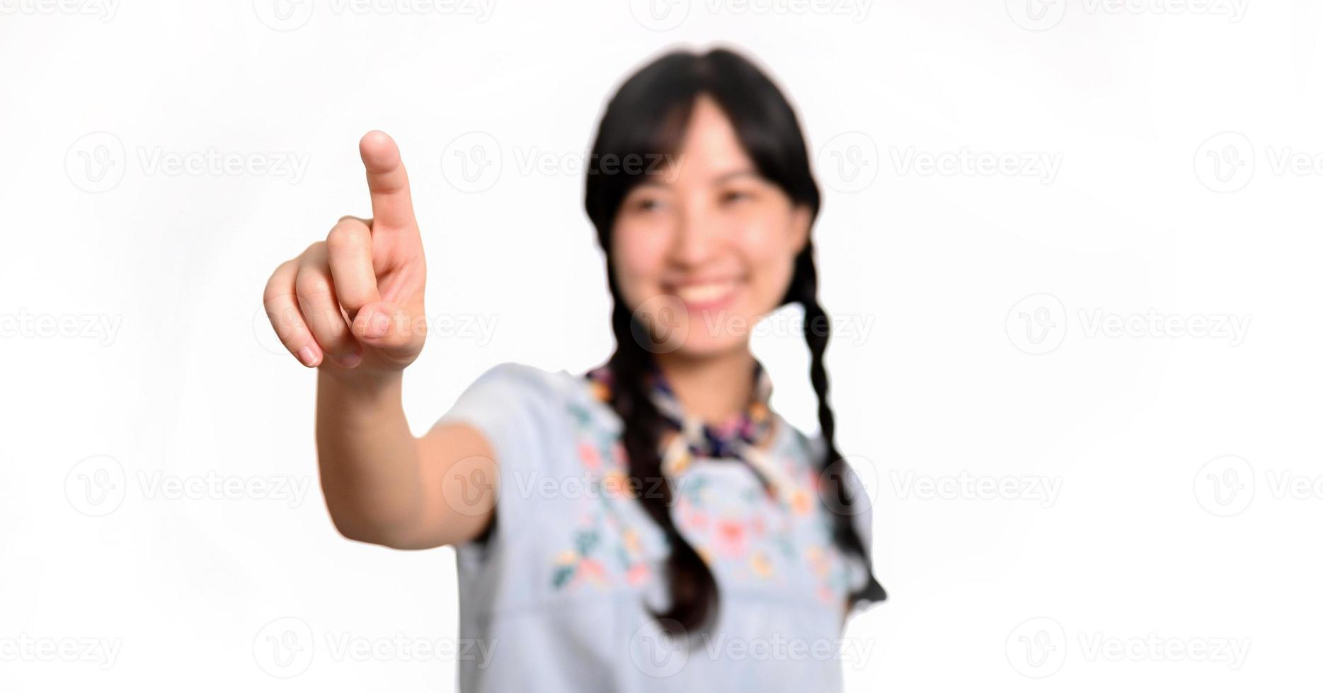 Portrait of beautiful happy young asian woman in denim dress touching invisible screen on white background. photo