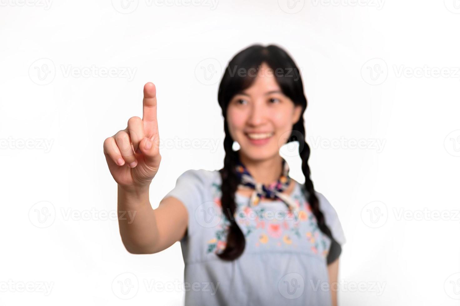 Portrait of beautiful happy young asian woman in denim dress touching invisible screen on white background. photo