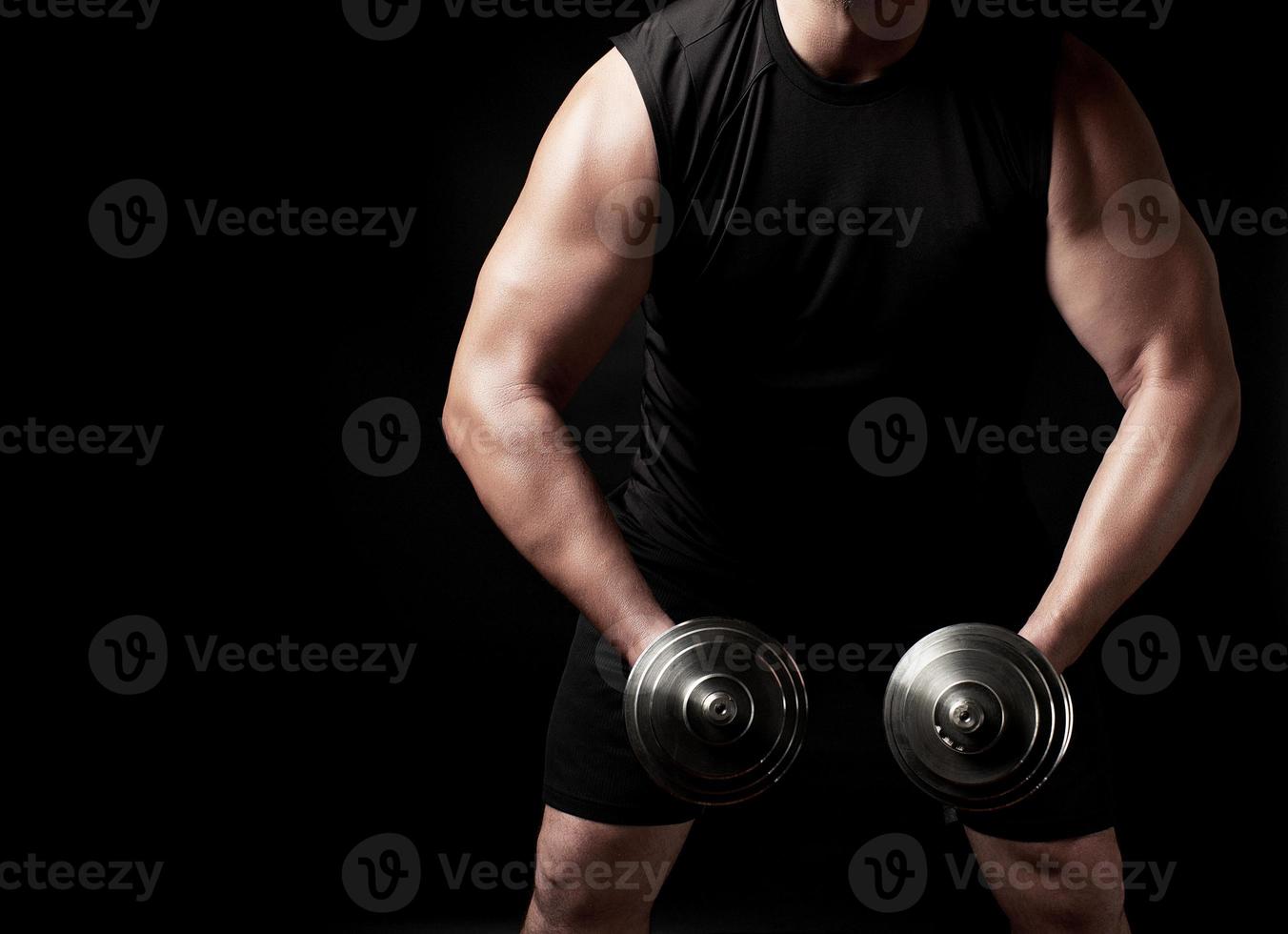 man in black clothes holds steel dumbbells in his hands, his muscles are tense photo