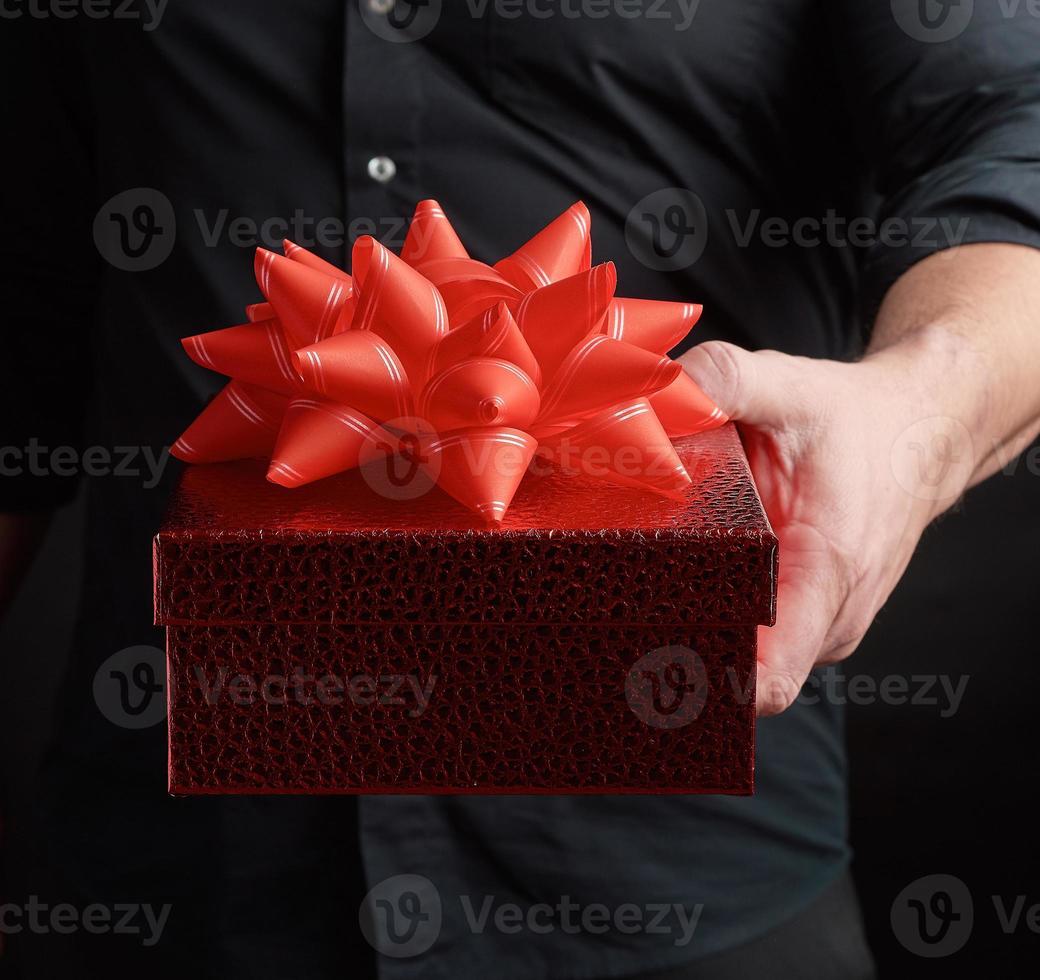 adult man in a black shirt holds a red square box with a knotted bow photo
