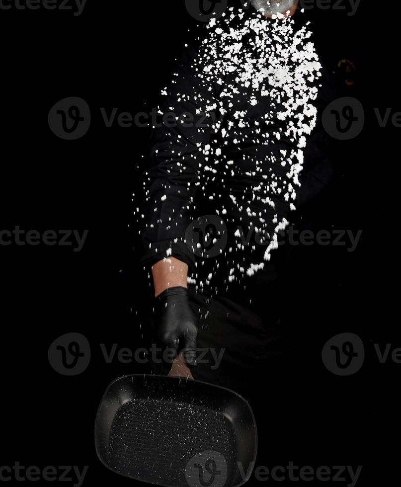 Chef in black uniform holds a pan with white salt and throws up photo