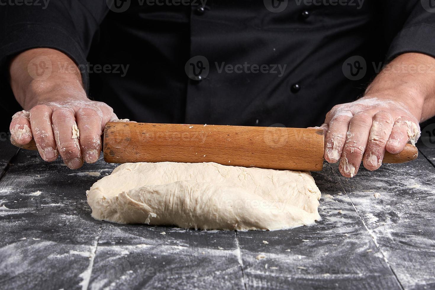 chef con túnica negra hace rodar una masa para una pizza redonda foto