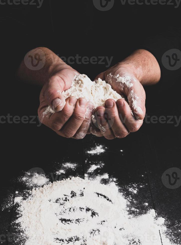 white wheat flour in male hands, black background photo