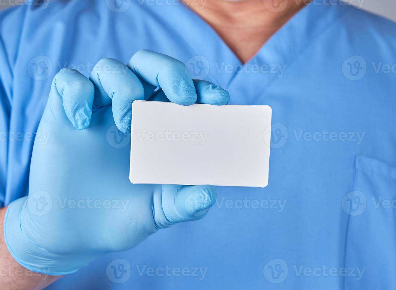 male doctor wearing blue latex gloves is holding a blank white paper business card photo