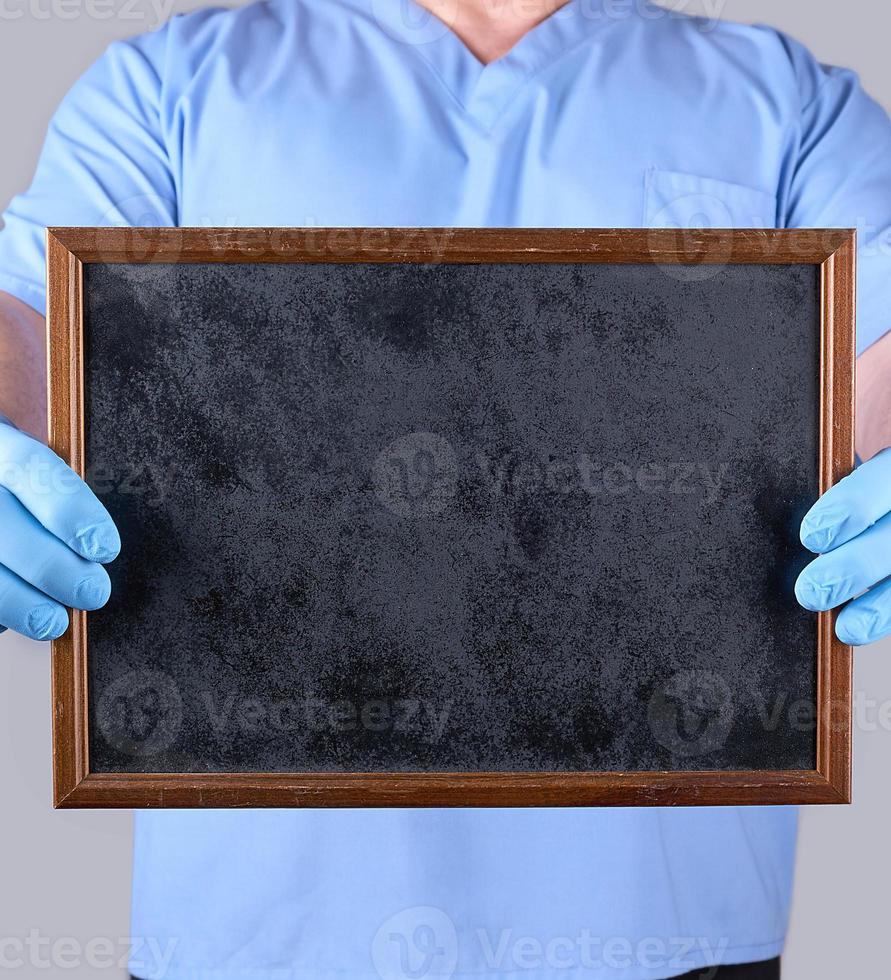 doctor in blue uniform and latex sterile gloves holding a blank black frame photo